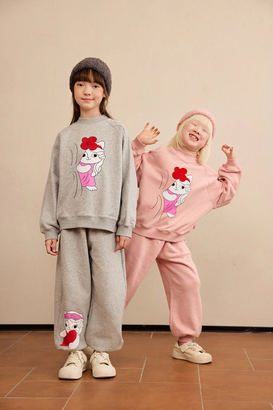 Two children in the Hide-and-Seek Cat sweatshirt and joggers, one in grey and one in pink.